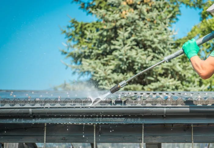 Photographie d'une personne qui nettoie une toiture avec un jet haut de pression