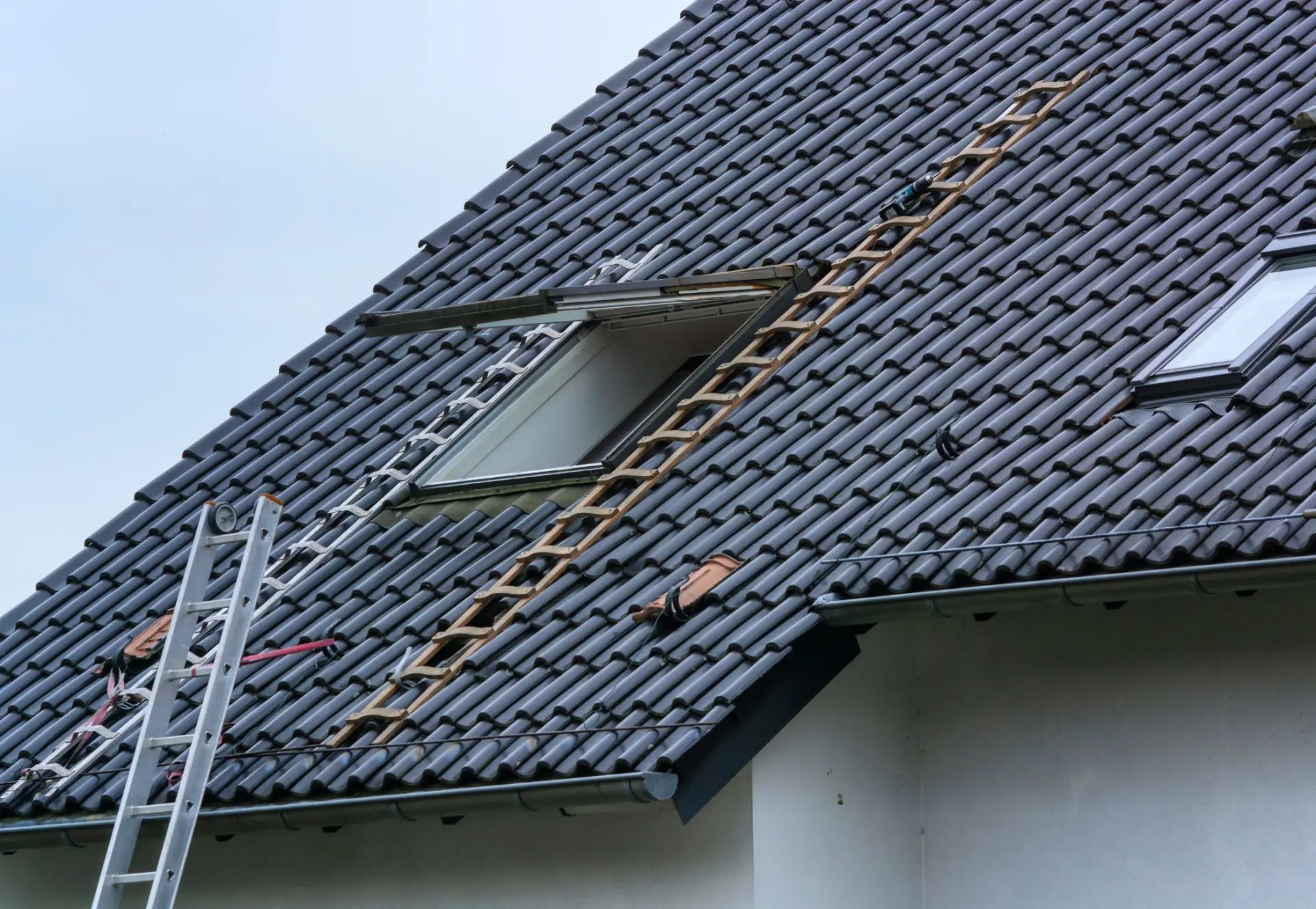 Tuiles de toit noires avec une échelle montrant un processus de rénovation de toiture